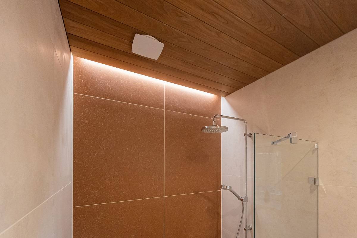 La iluminación de acento en la pared del fondo de la ducha con tiras de LED aporta una hermosa luz a un espacio en la ranura de un techo panelado que se ha dejado desnudo.